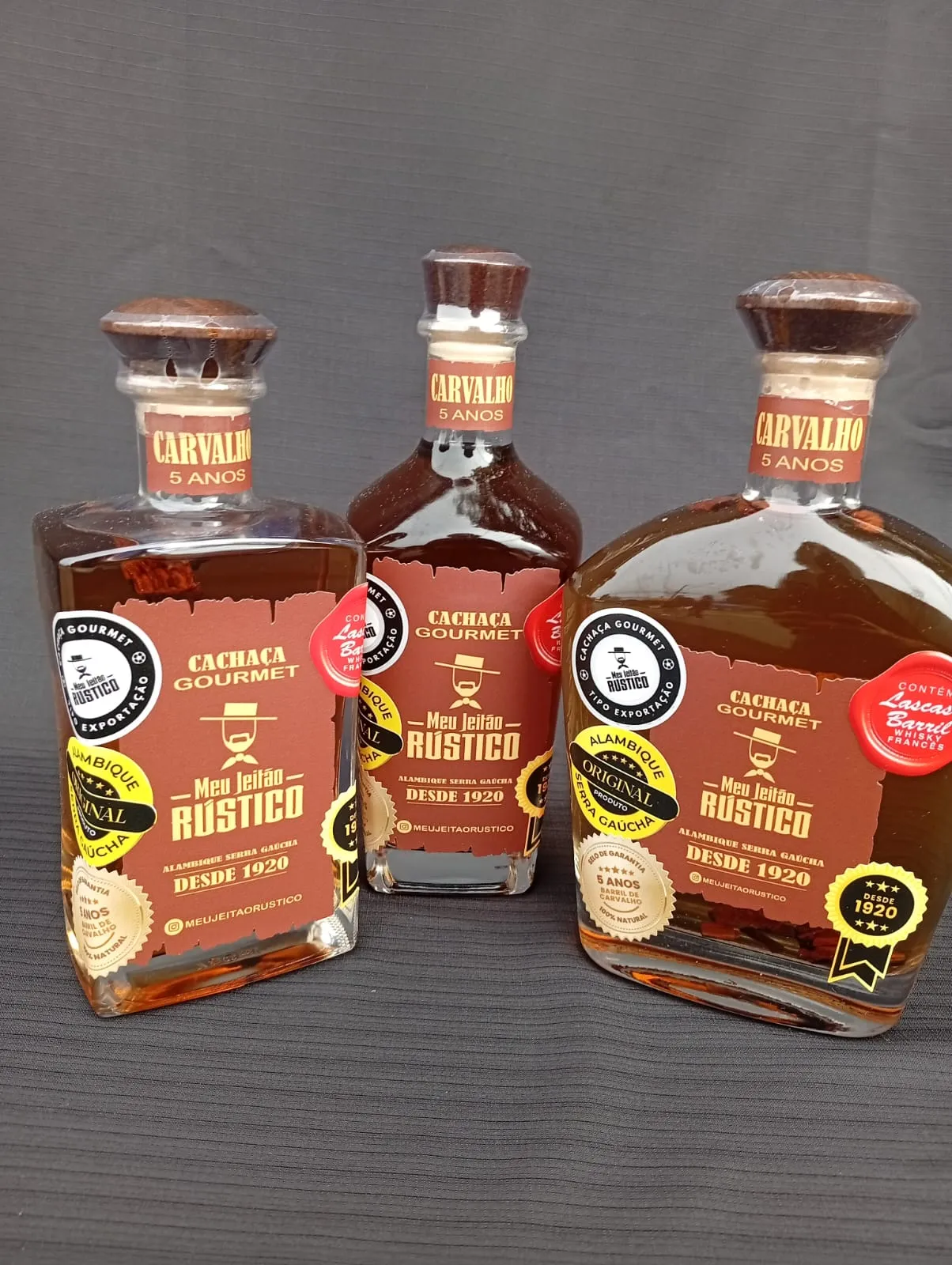 Três garrafas de cachaça premium sabor carvalho de 750 ml em formatos diferentes, lado a lado